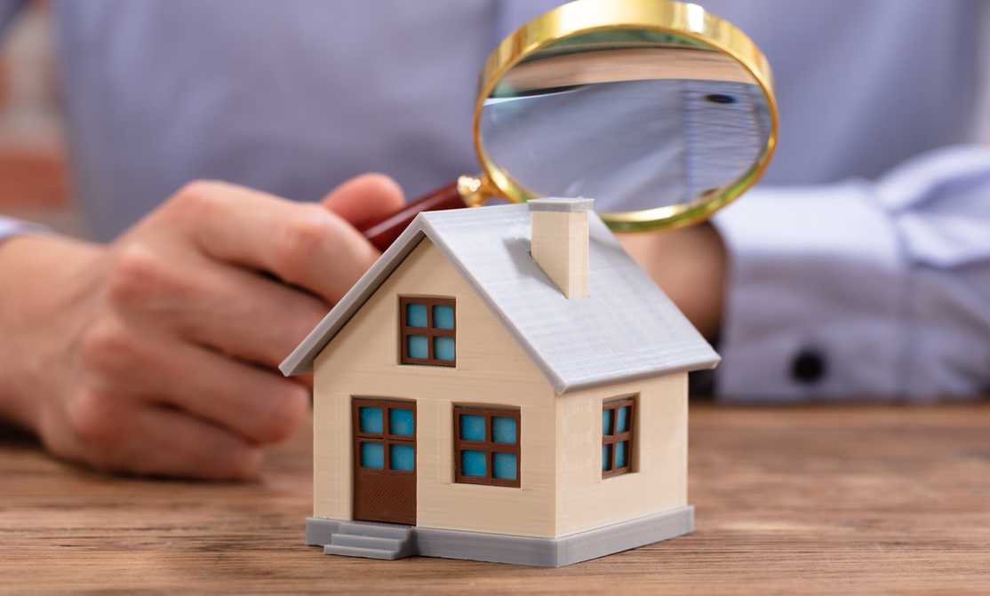 man looking at a model house with a magnifying glass 